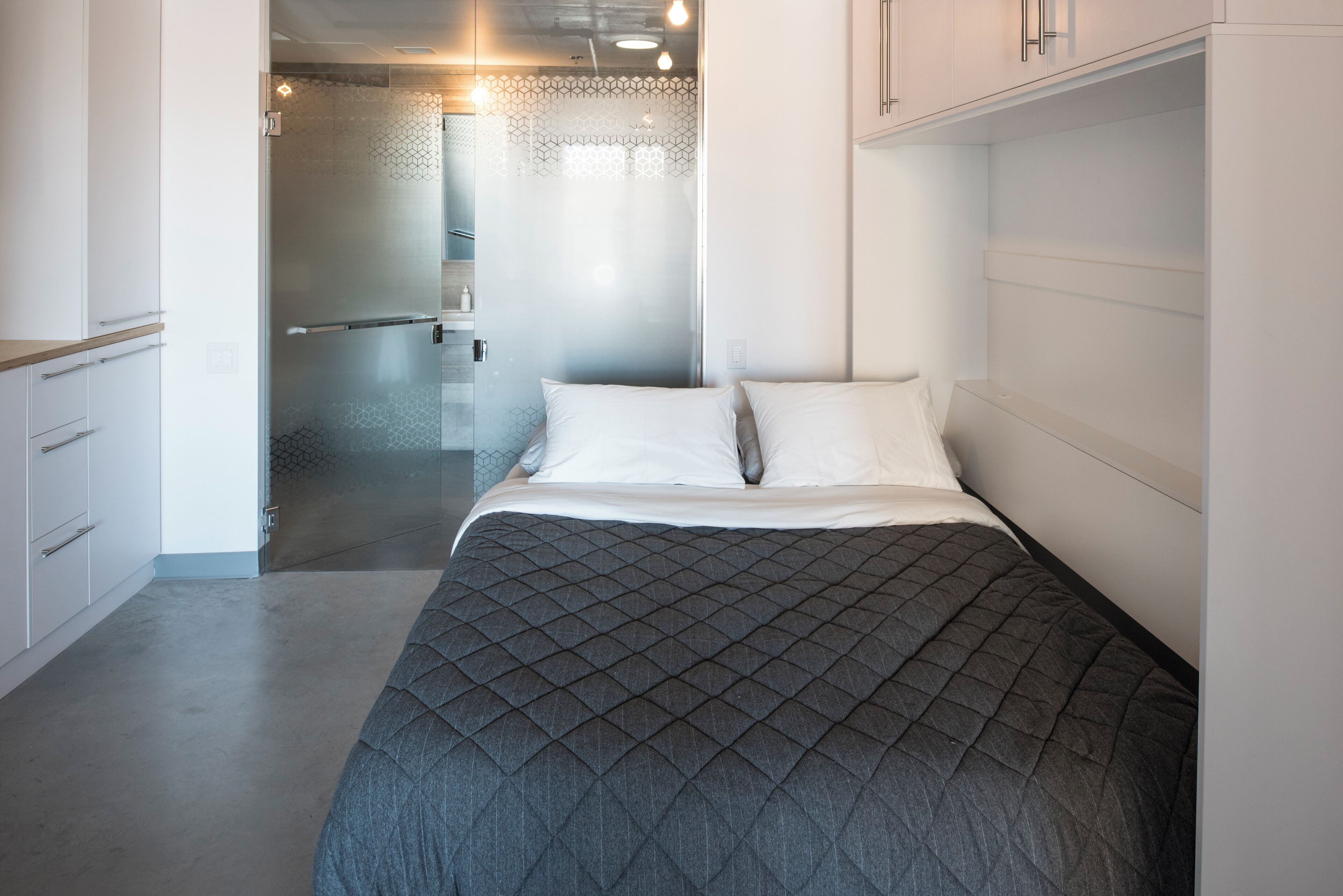 Un dormitorio con cama, vestidor y baño con puerta de vidrio.