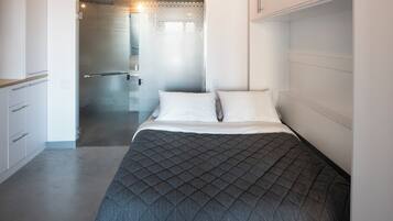 Un dormitorio con cama, vestidor y baño con puerta de vidrio.