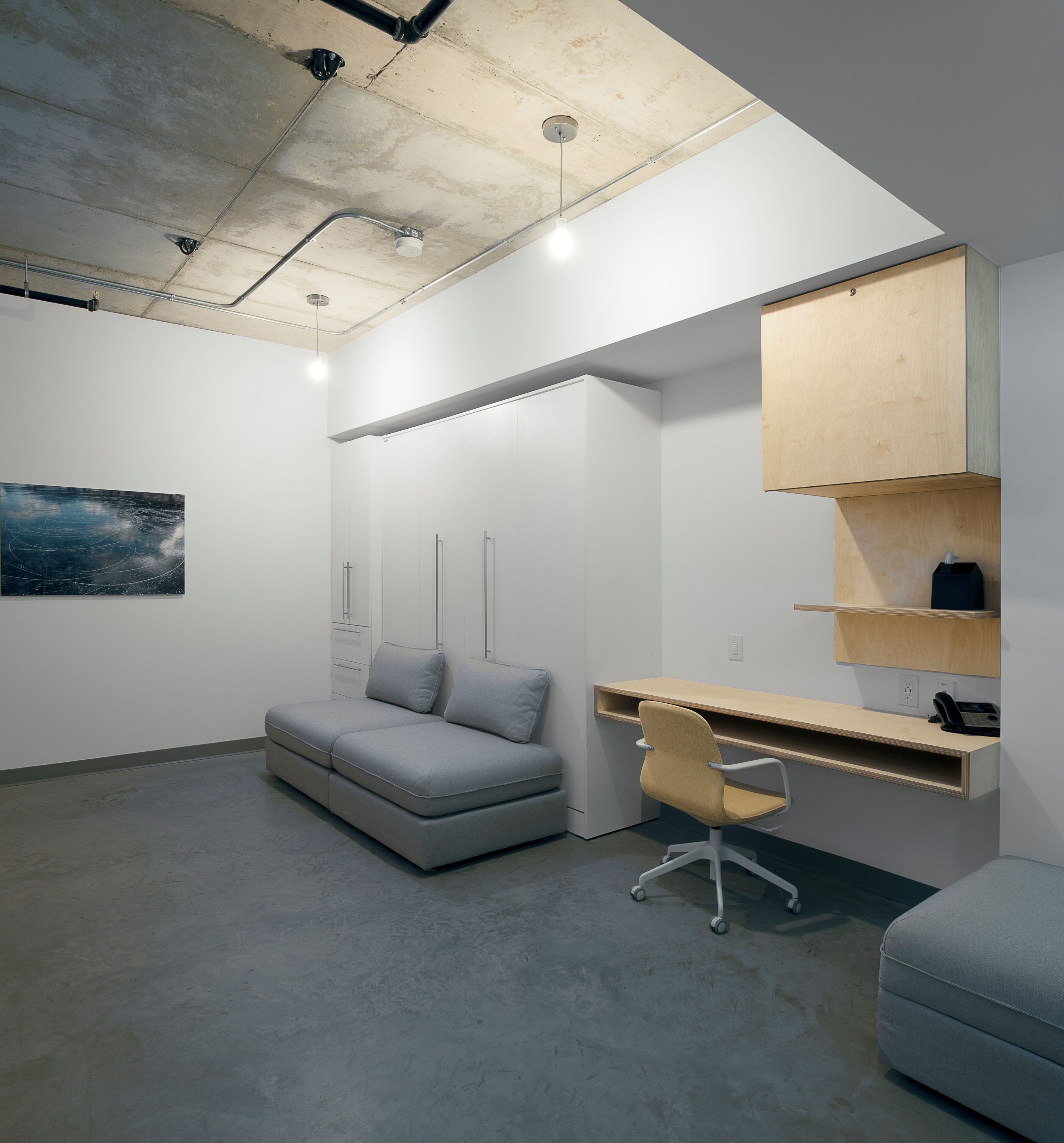 Un espacio de oficina moderno con un sofá gris, un escritorio blanco y una estantería de madera.