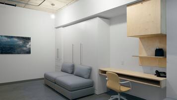 Un espacio de oficina moderno con un sofá gris, un escritorio blanco y una estantería de madera.