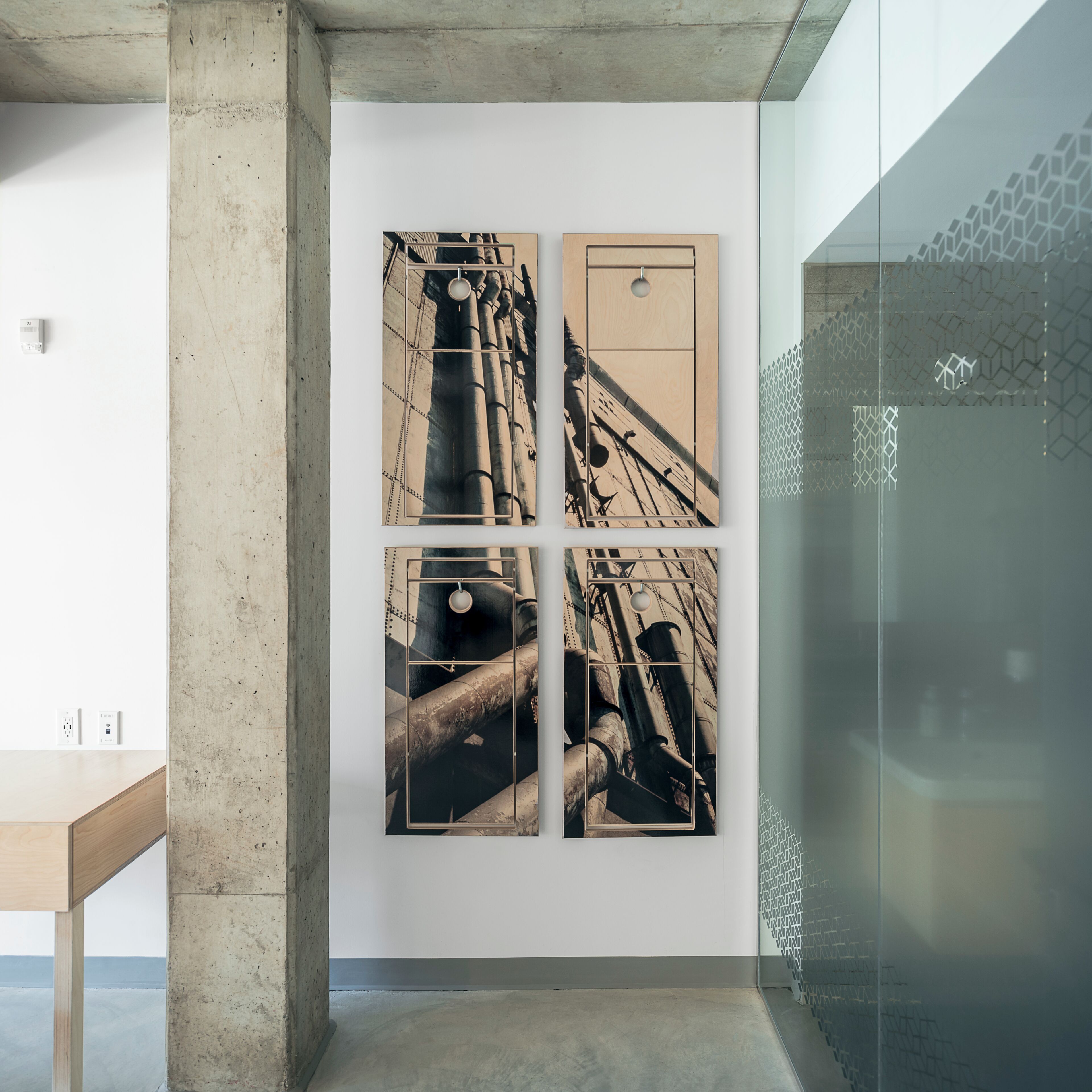 Un interior moderno con un pilar de concreto, una partición de vidrio y una obra de arte en la pared que representa estructuras industriales.