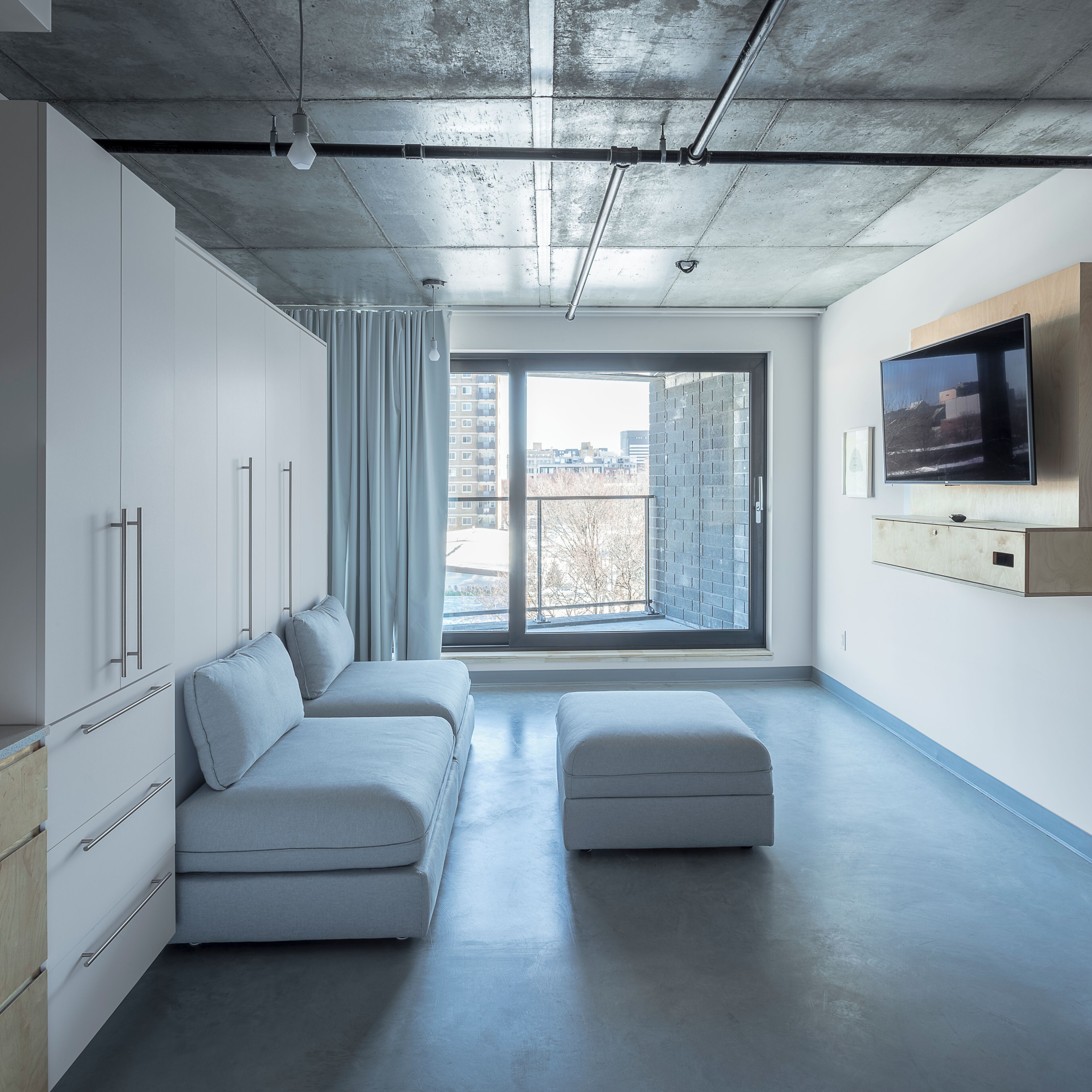 A modern living room with a sofa, ottoman, and a TV mounted on the wall.