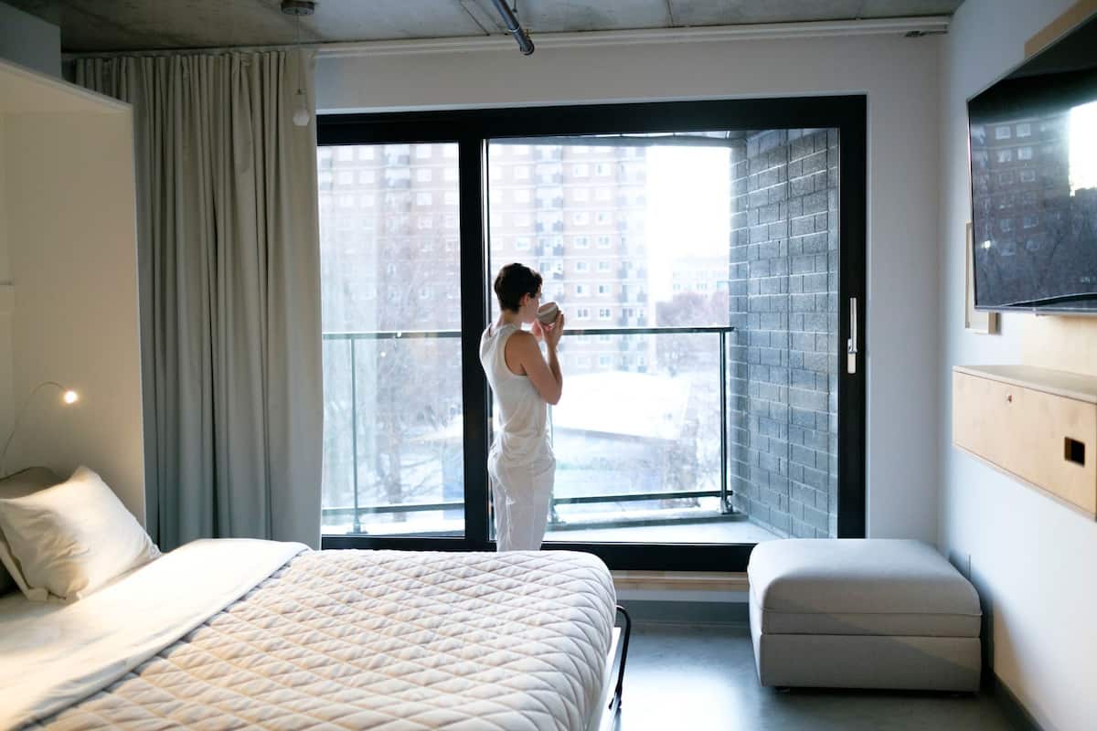 A hotel room with a large bed, a window with a view of buildings, and a small seating area.