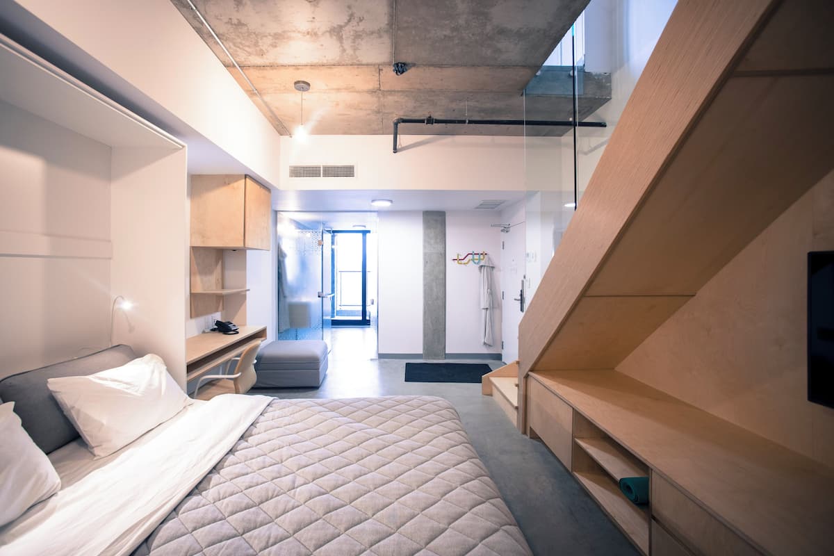 A modern hotel room with a large bed, a desk, and a walk-in closet.