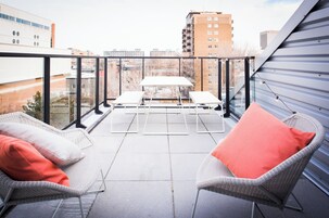 Un balcon avec deux fauteuils en osier, une petite table et une rambarde en verre.