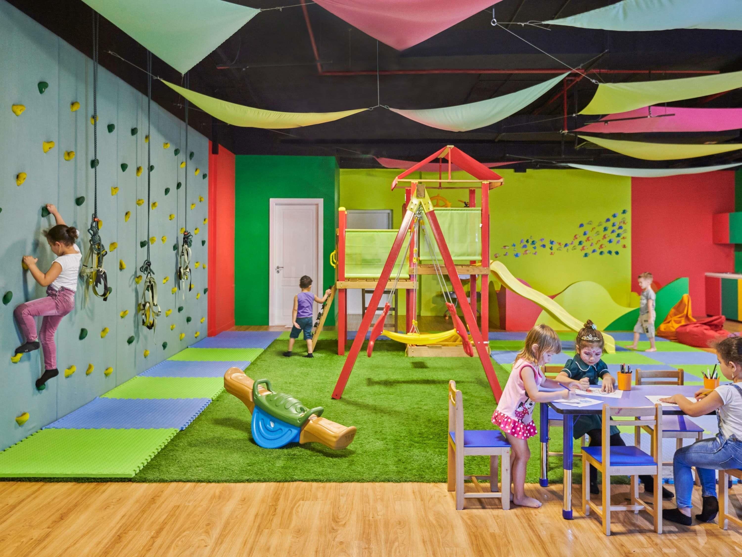 A children's play area with climbing walls, a swing set, and a table with children painting.