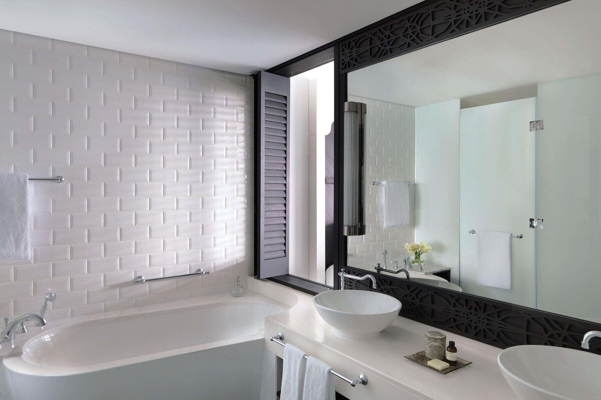A modern bathroom with a large bathtub, two sinks, and a large mirror.