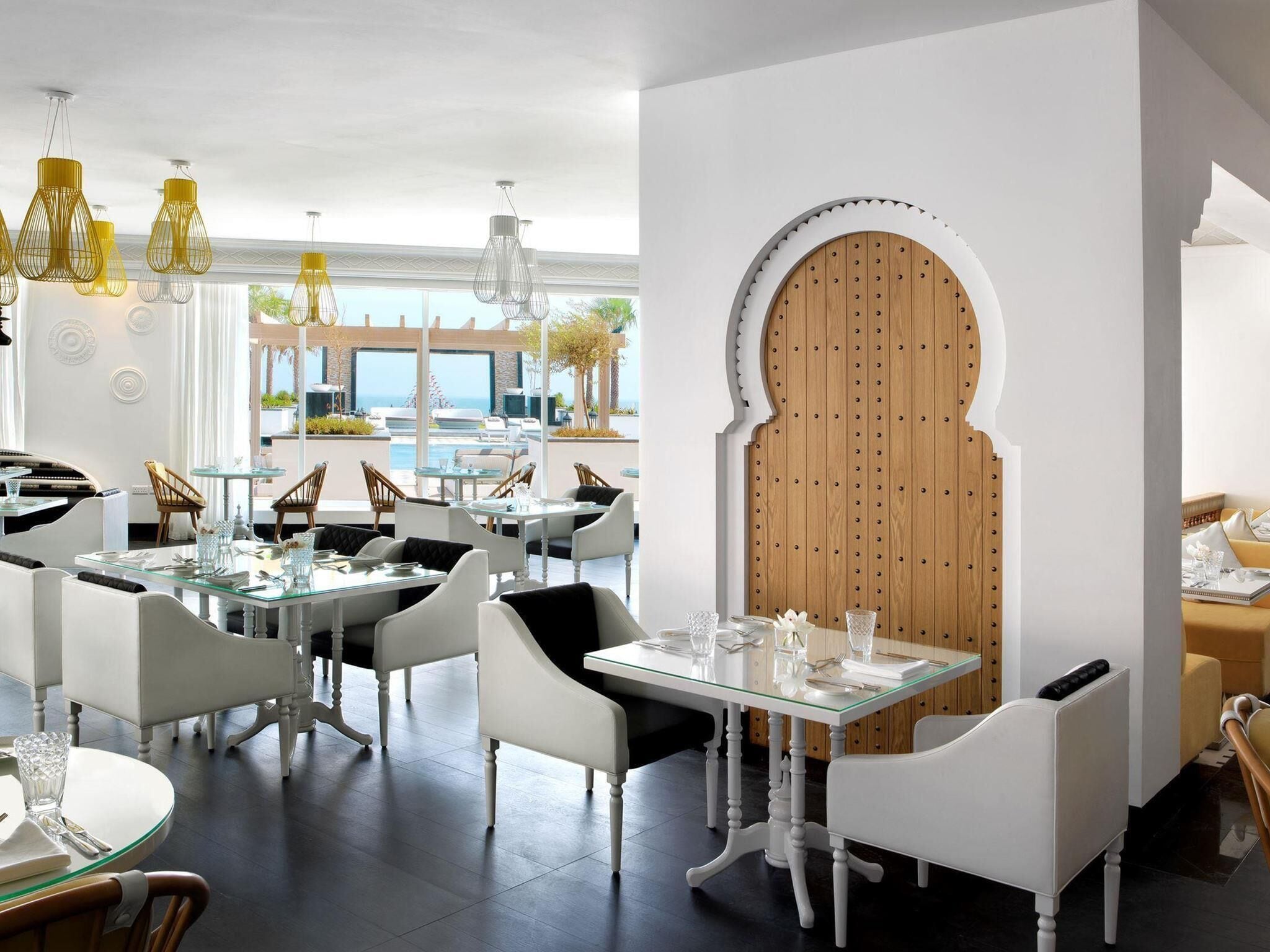 A modern dining area with glass tables, white chairs, and hanging light fixtures.