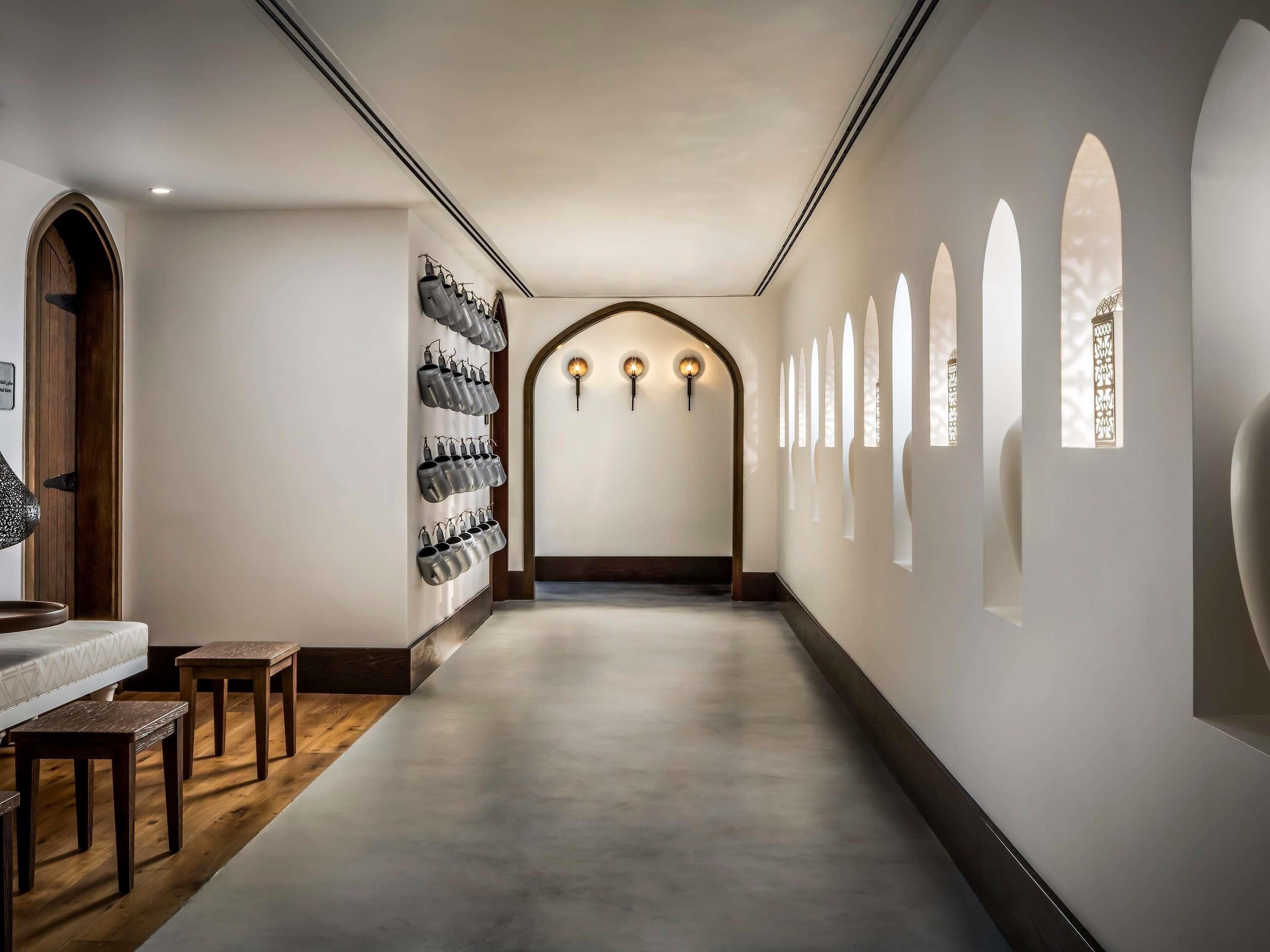A hallway with a wooden floor, a wall-mounted coat rack, and a series of arched windows.