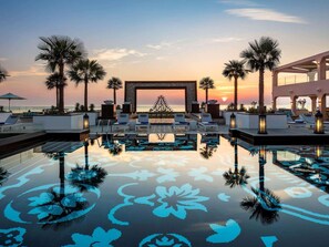 Un espace aménagé au bord de la piscine, avec des chaises longues, des palmiers et une vue imprenable sur le coucher de soleil.