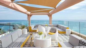 A rooftop lounge with outdoor seating, a glass balustrade, and a view of the ocean. - Fairmont Fujairah Beach Resort (Dibba)