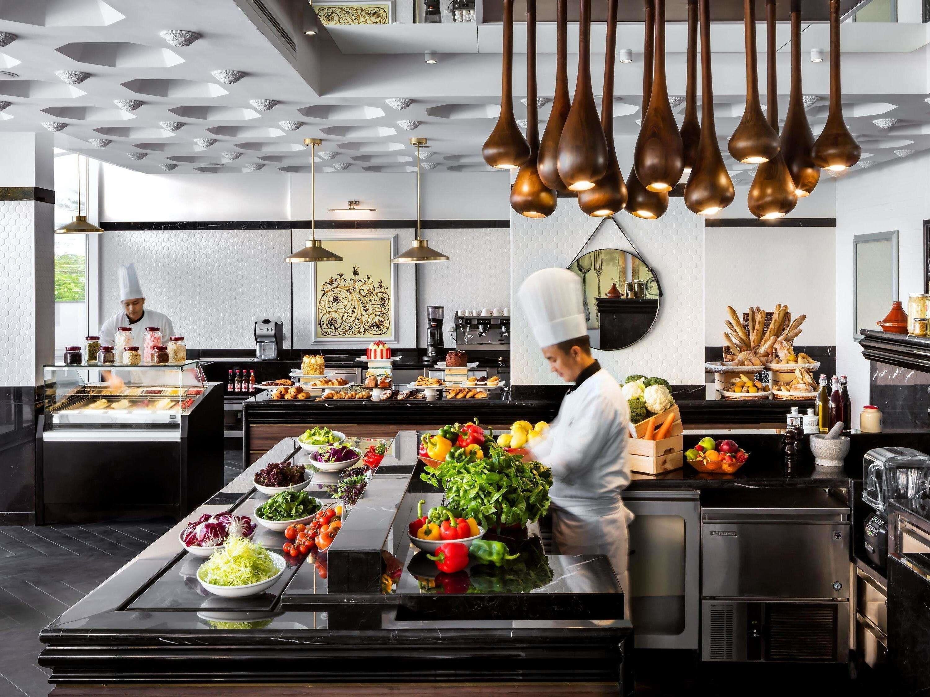 Una cocina moderna con un chef preparando alimentos, un bufé con diversos platos y un diseño de techo elegante.