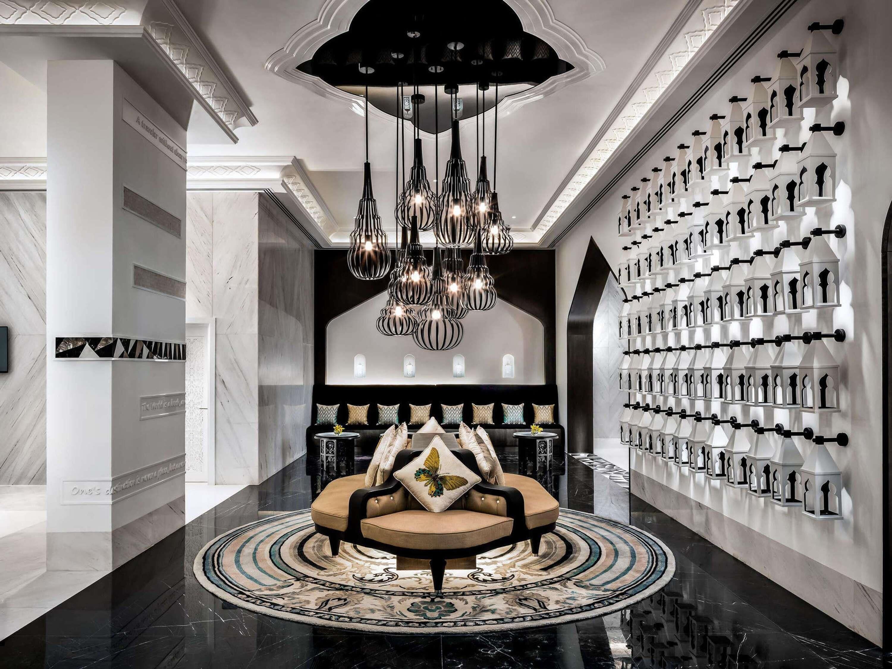 A modern lobby with a central seating area, a chandelier, and a wall of decorative bottles.