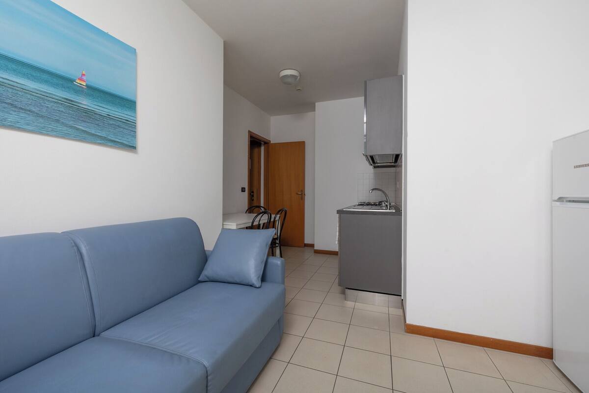 Ein Wohnzimmer mit einer Couch, ein Essbereich mit Stühlen, eine Küche mit Kühlschrank und eine Tür zu einem anderen Raum.