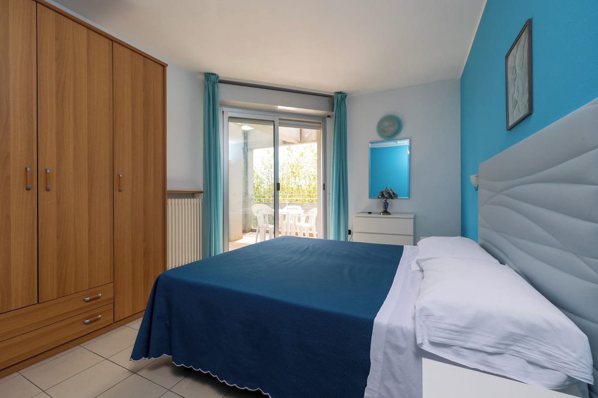 Ein Schlafzimmer mit Bett, Schrank, Schreibtisch und Blick ins Freie.