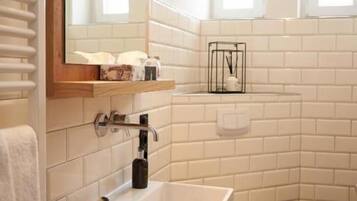 Un baño moderno con azulejos blancos tipo metro, un lavamanos blanco, un inodoro y un espejo con dos lámparas colgantes negras.