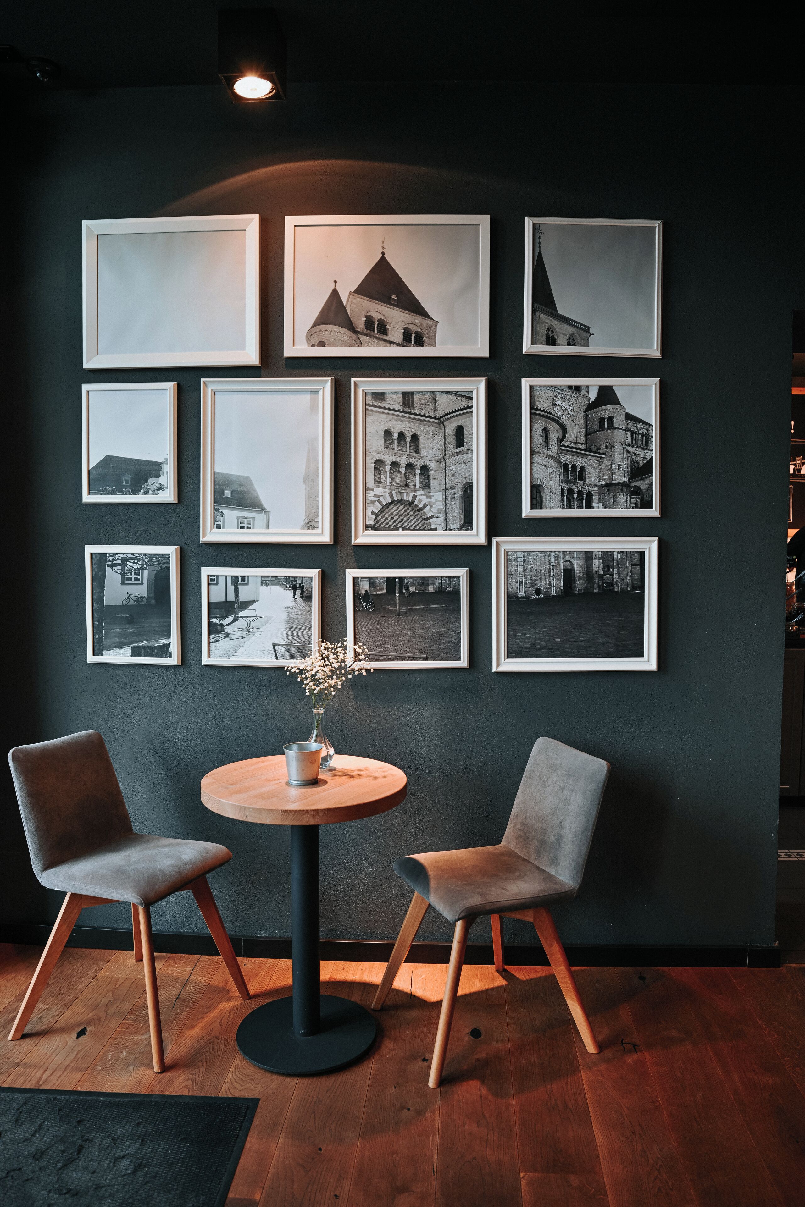 A room with a dark wall, a round table, two chairs, and multiple framed pictures.