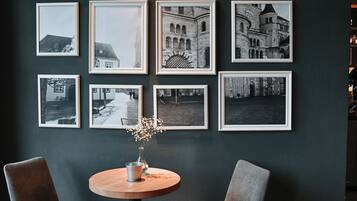 A room with a dark wall, a round table, two chairs, and multiple framed pictures.