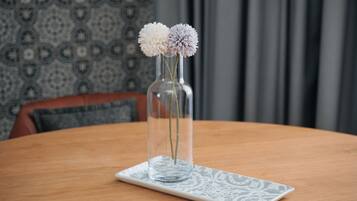 A clear glass vase with two flowers on a white plate on a wooden table.