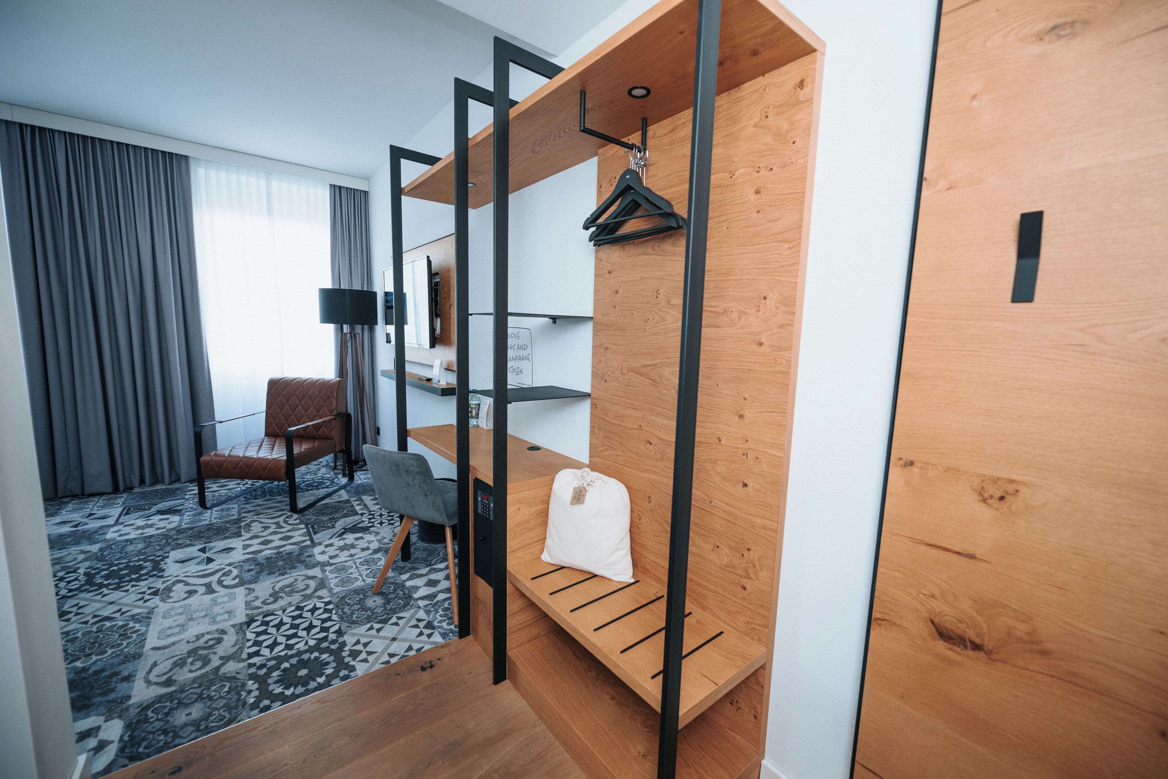 Een moderne hotelkamer met een houten bankje, een kapstok, een stoel en een bureau.