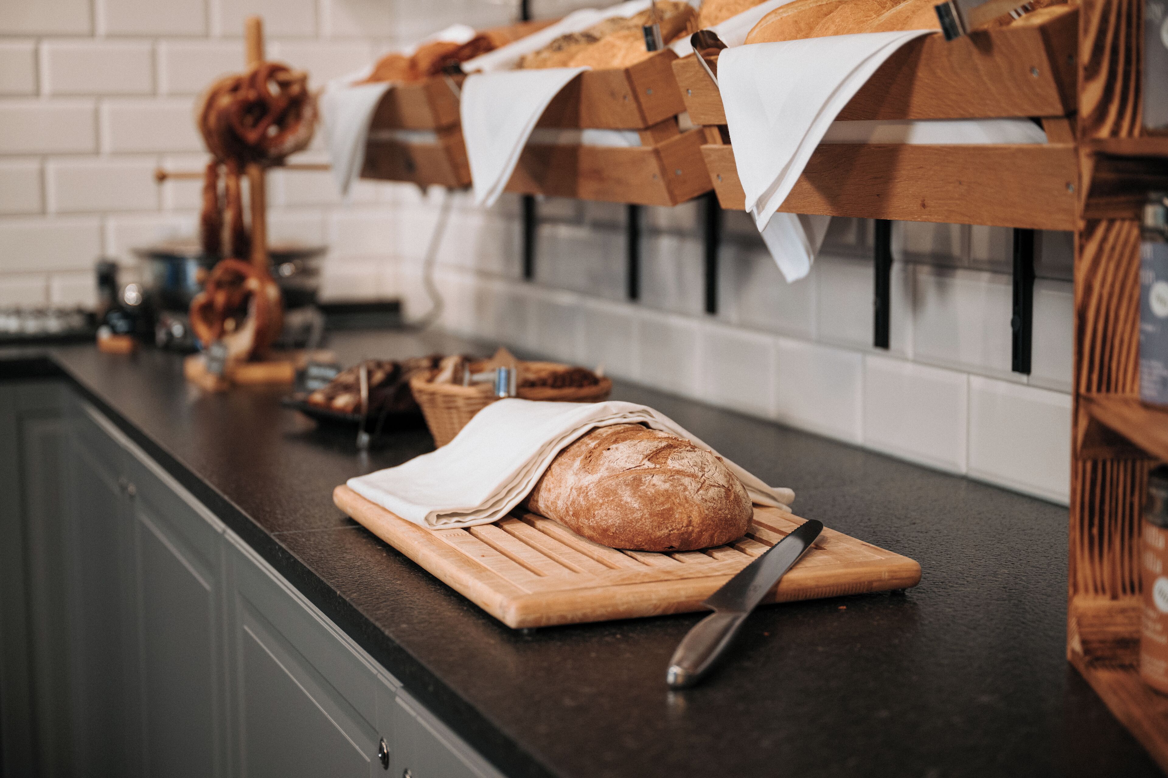 A kitchen counter with a loaf of bread on a cutting board, a knife, and bread baskets hanging above.