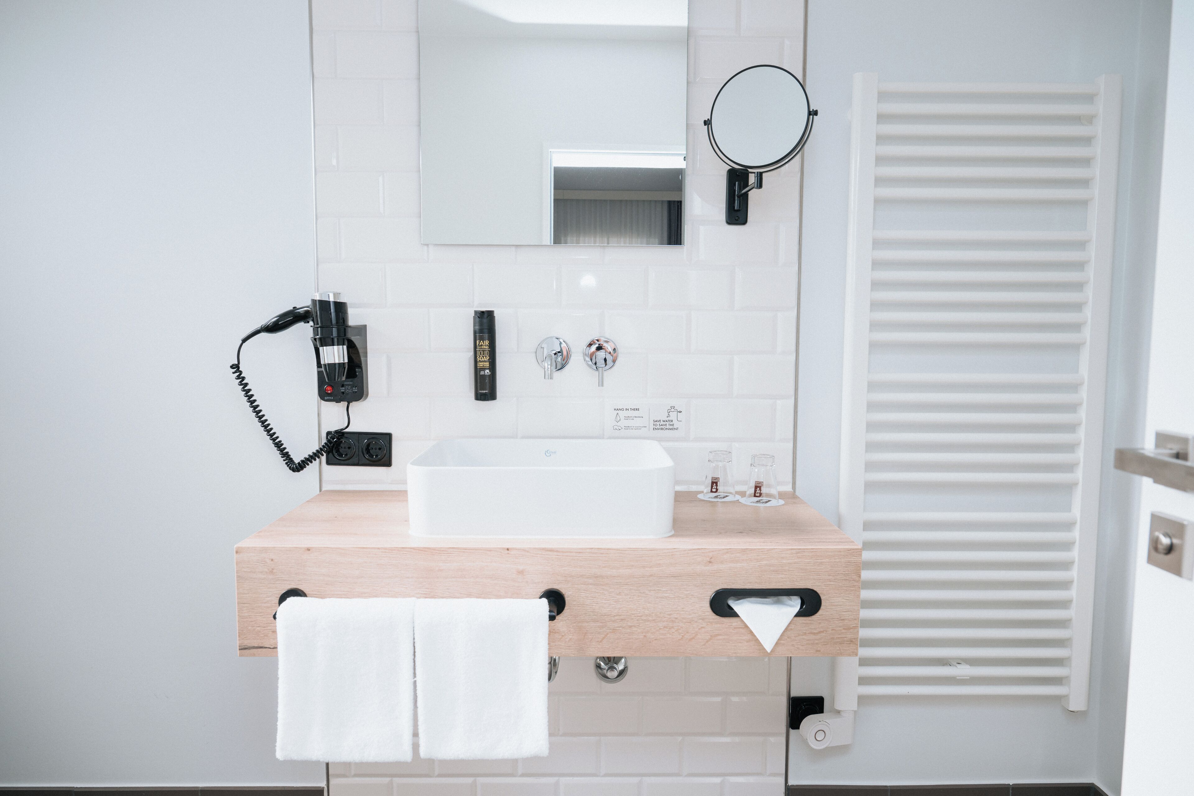 Ein modernes Badezimmer mit einem weißen Waschbecken, einem Spiegel, einem Handtuchhalter und einem darüber hängenden Handtuch.