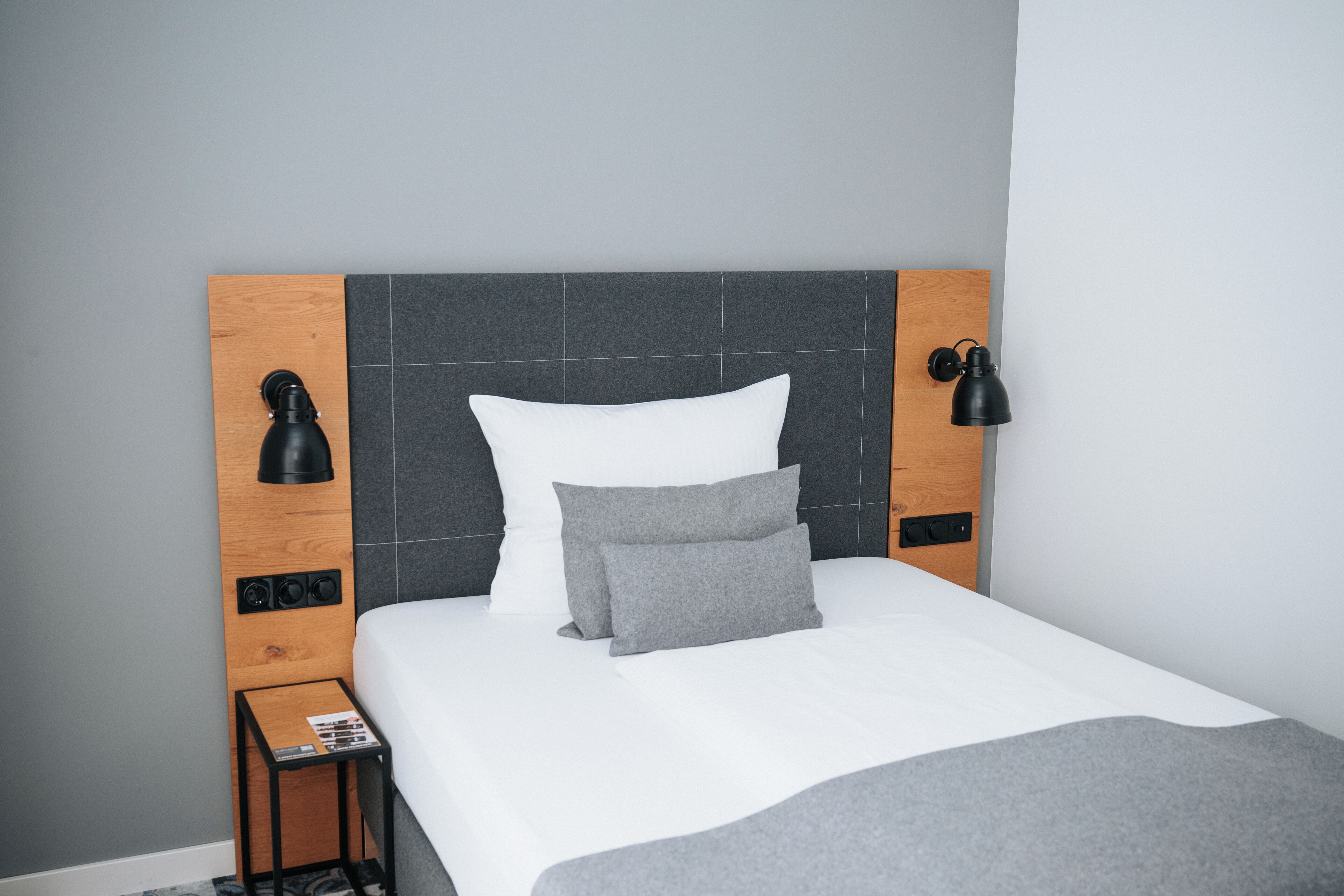 A neatly made bed with a wooden headboard, two bedside lamps, and a small table with a magazine.