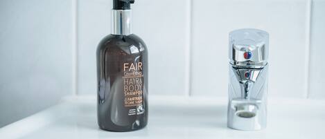 Casa de banho com um frasco de champô e gel de banho Fairtrade e uma torneira moderna.
