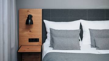 A neatly made bed with grey bedding, a wooden nightstand with a black lamp, and a grey headboard.