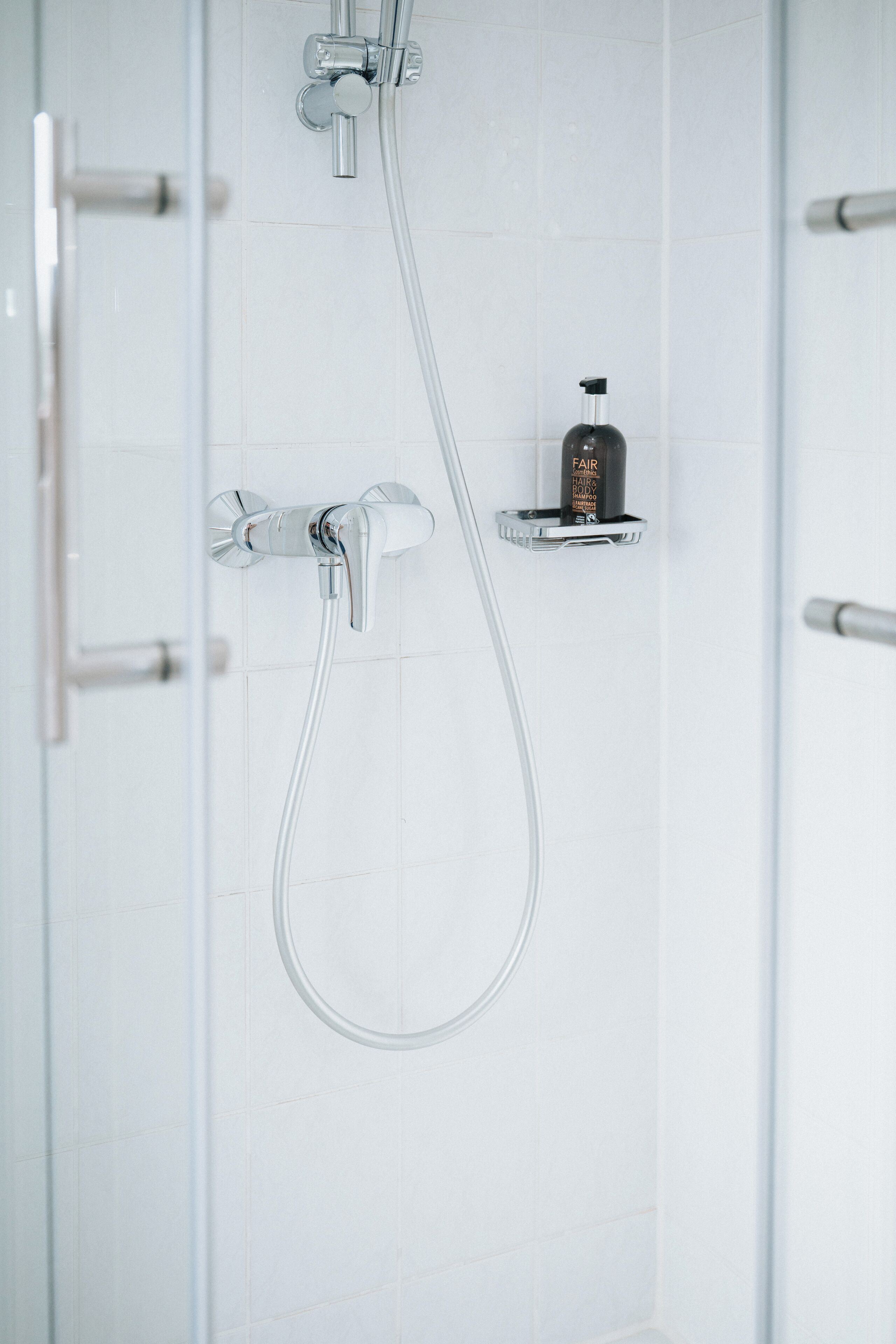 Une douche équipée d’un pommeau de douche à main et d’un robinet fixé au mur.