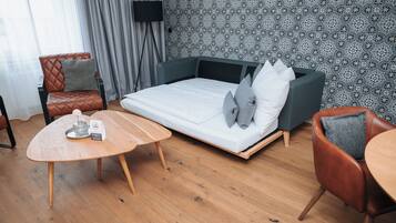 A modern room with a sofa bed, a wooden coffee table, a leather armchair, and a patterned wallpaper.