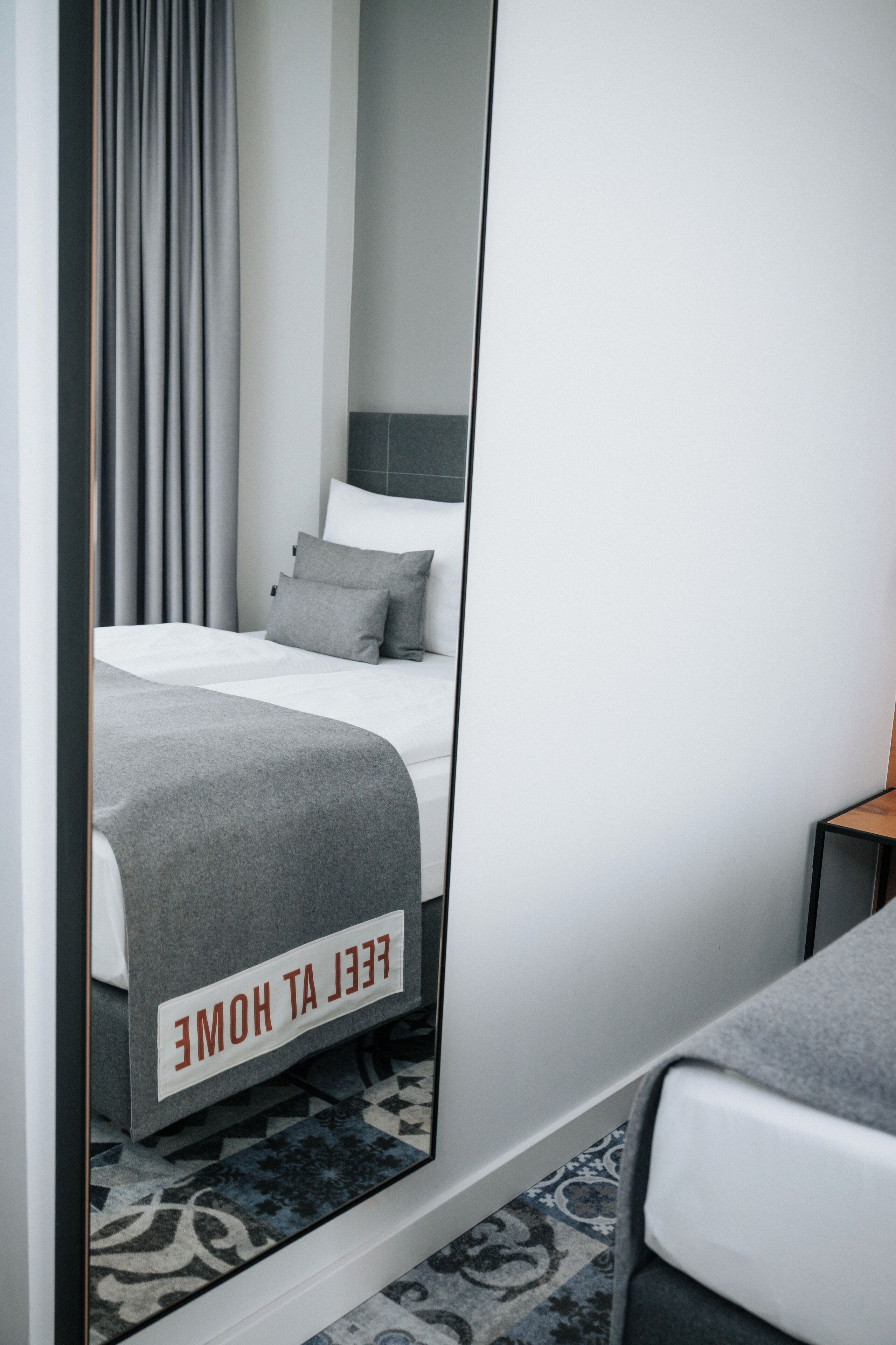 Habitación de hotel con cama, espejo que refleja la habitación, mesita de noche y un cartel sobre la cama.
