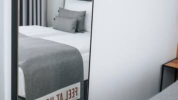 Habitación de hotel con cama, espejo que refleja la habitación, mesita de noche y un cartel sobre la cama.