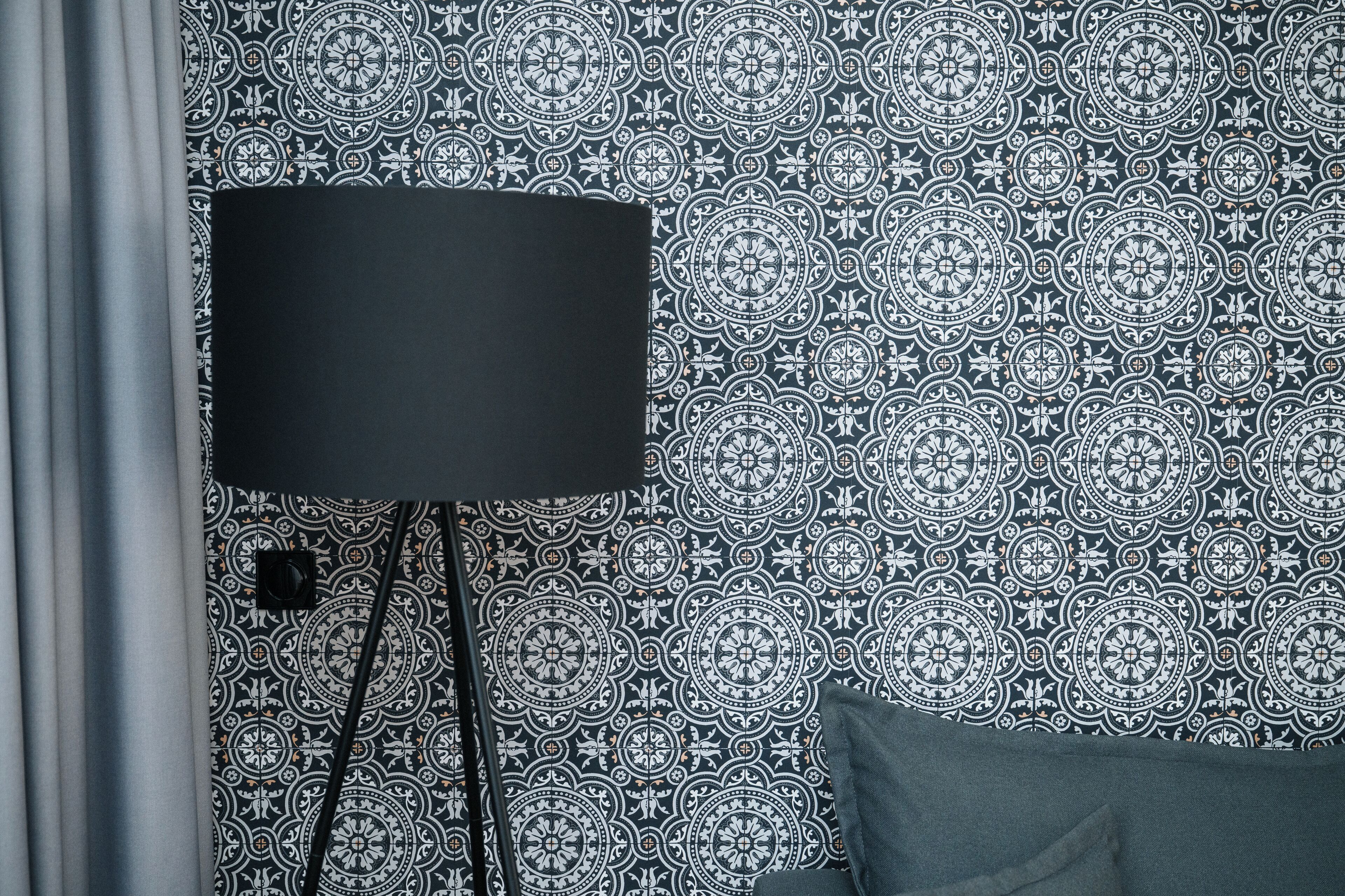 A room with a patterned wallpaper, a black floor lamp, and a dark-colored sofa.