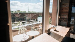 Un restaurante con vistas a un puente sobre un río, mesas y sillas de madera.