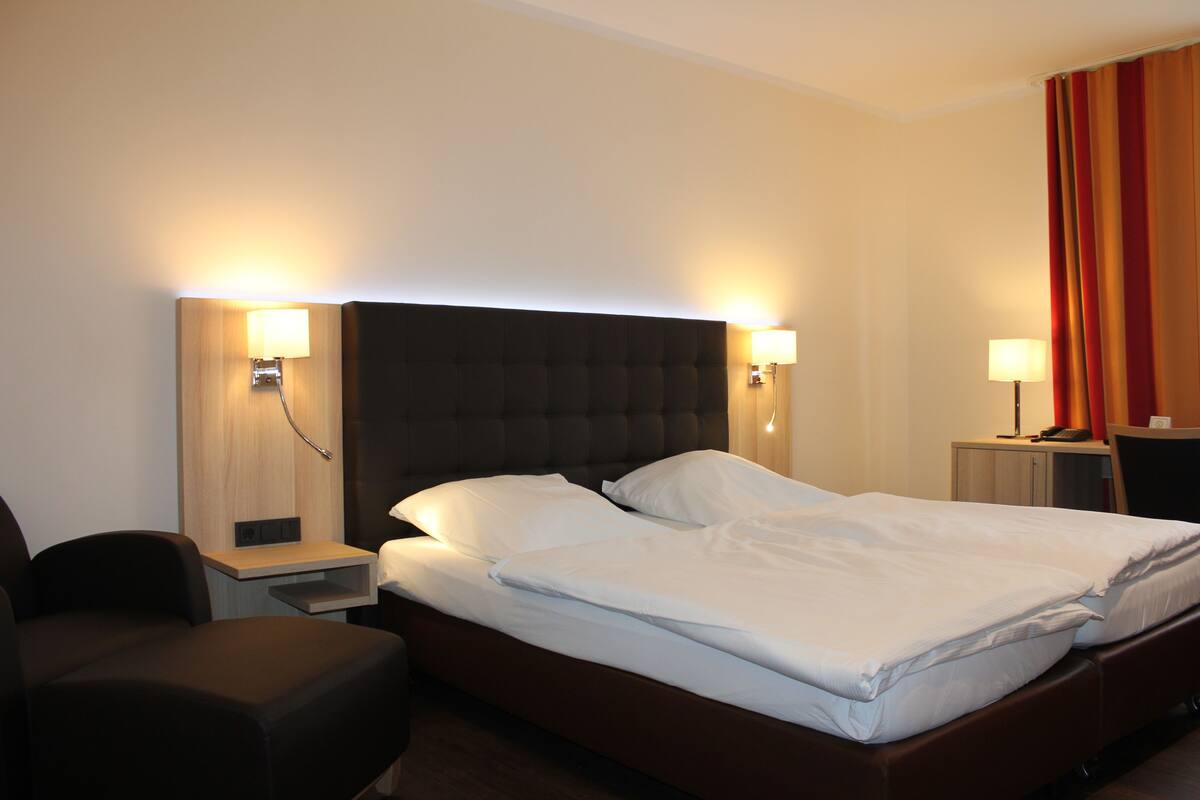 Una habitación de hotel con una cama grande, dos mesitas de noche, una silla y un escritorio.