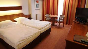 A hotel room with two beds, a small round table with chairs, a television, and a painting on the wall.