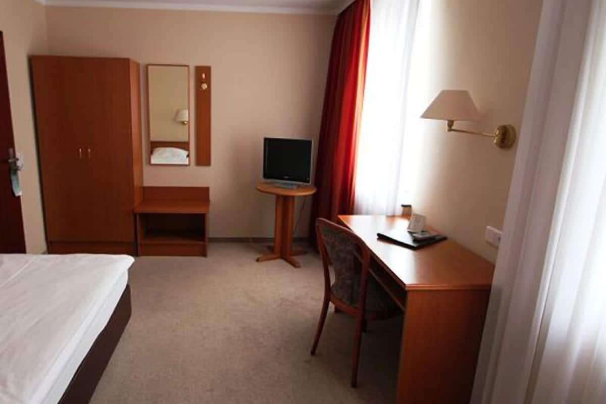 Habitación de hotel con cama, escritorio con silla, televisor, espejo y ventana con cortinas.