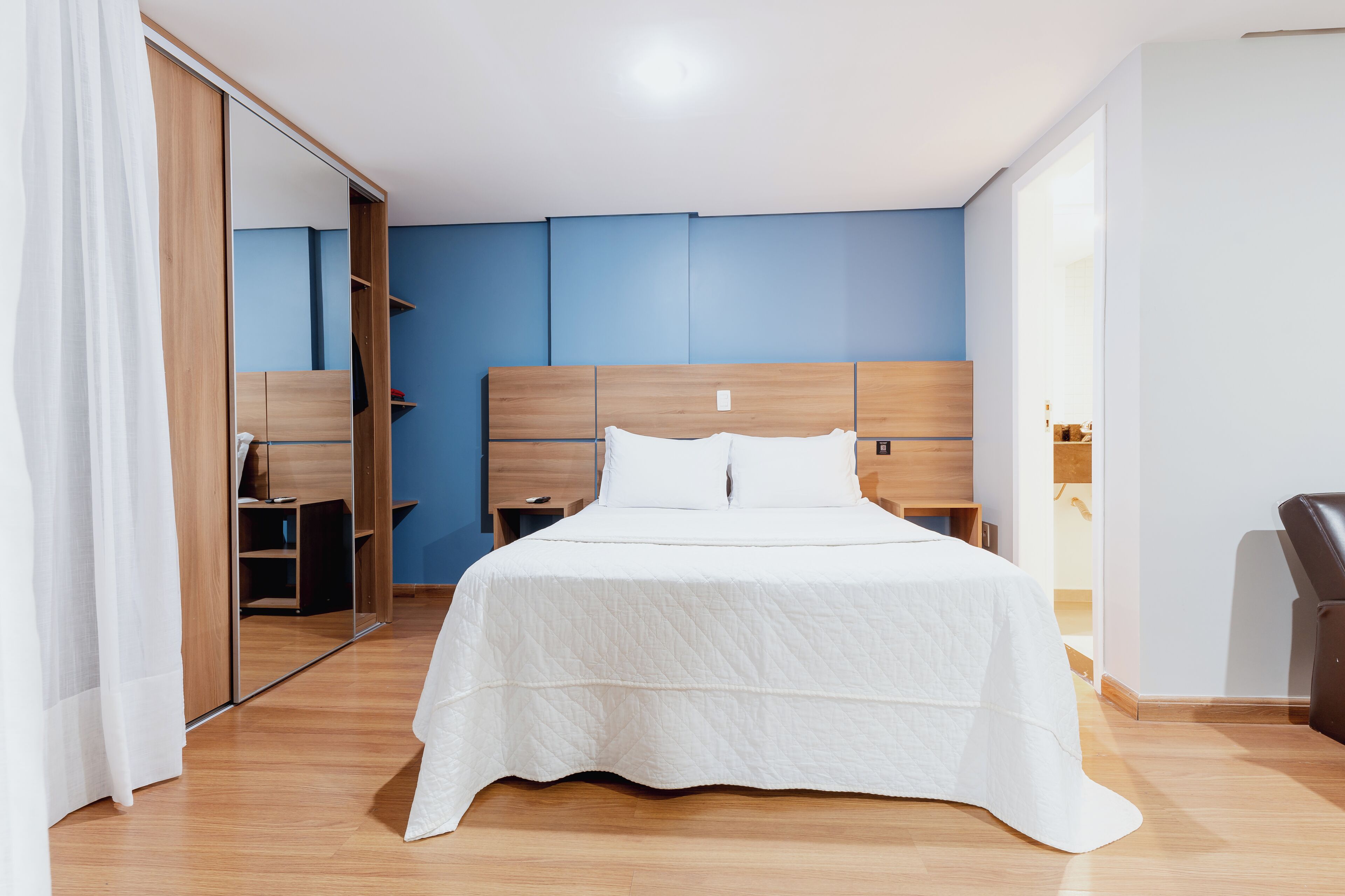 A bedroom with a wooden headboard, a white bedspread, and a mirror cabinet.