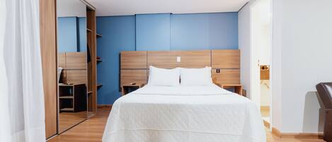 A bedroom with a wooden headboard, a white bedspread, and a mirror cabinet.