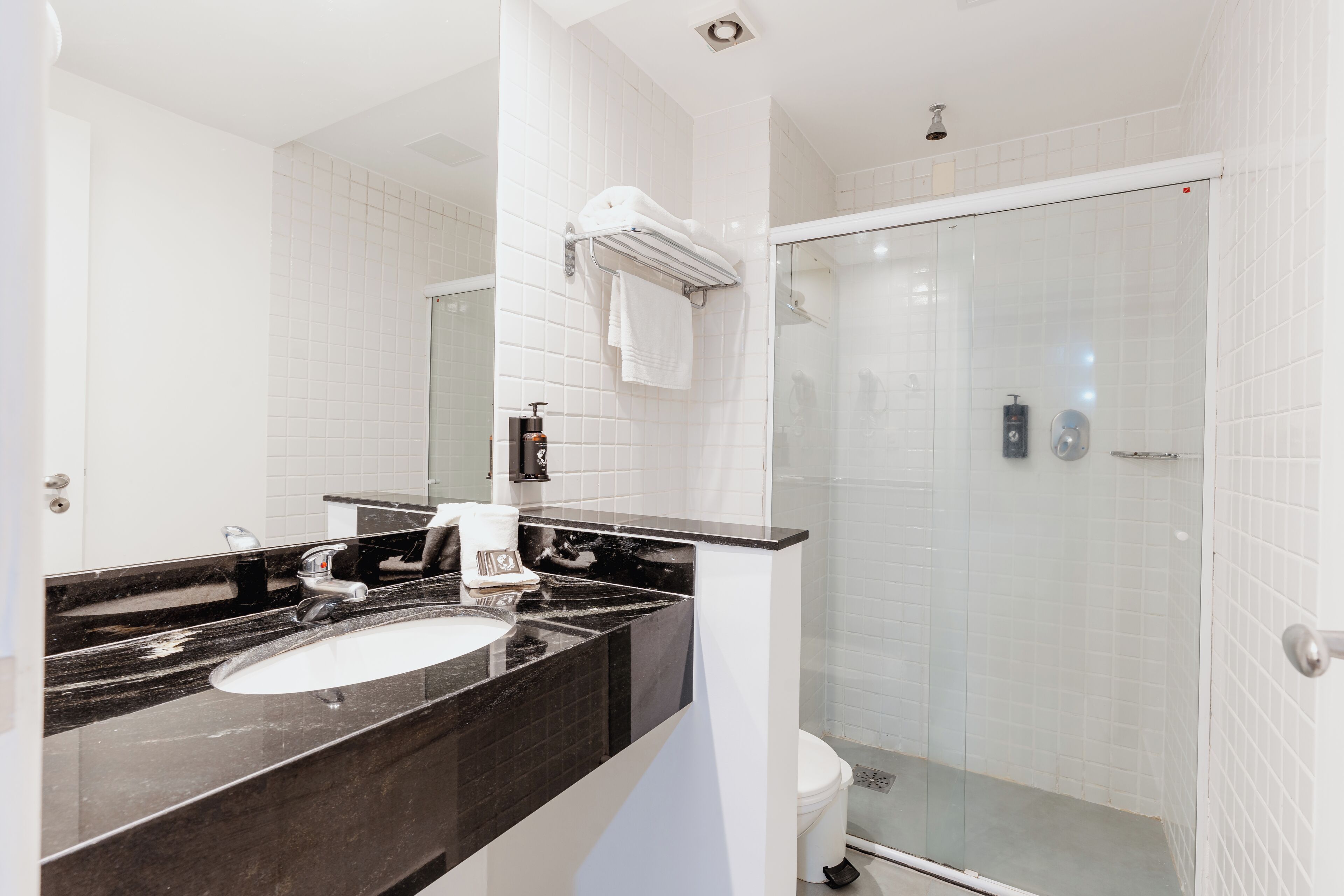 A modern bathroom with a black marble sink, white tiles, a glass shower enclosure, and a towel rack.