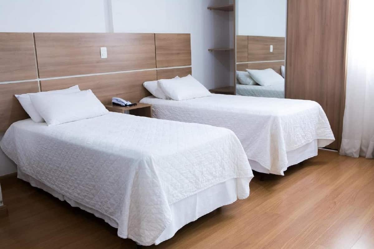 A hotel room with two beds, wooden headboards, white bedding, a bedside table with a phone, and a mirror.