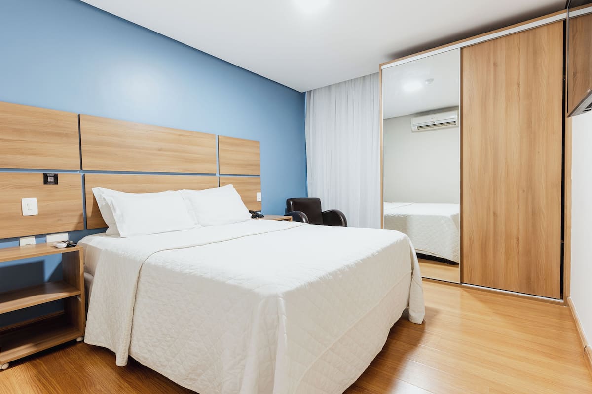 A modern hotel room with a large bed, wooden headboard, and a sliding door closet.