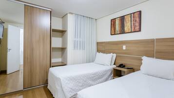 Quarto de hotel com duas camas, um guarda-roupa, uma mesa de cabeceira com telefone e um quadro na parede.