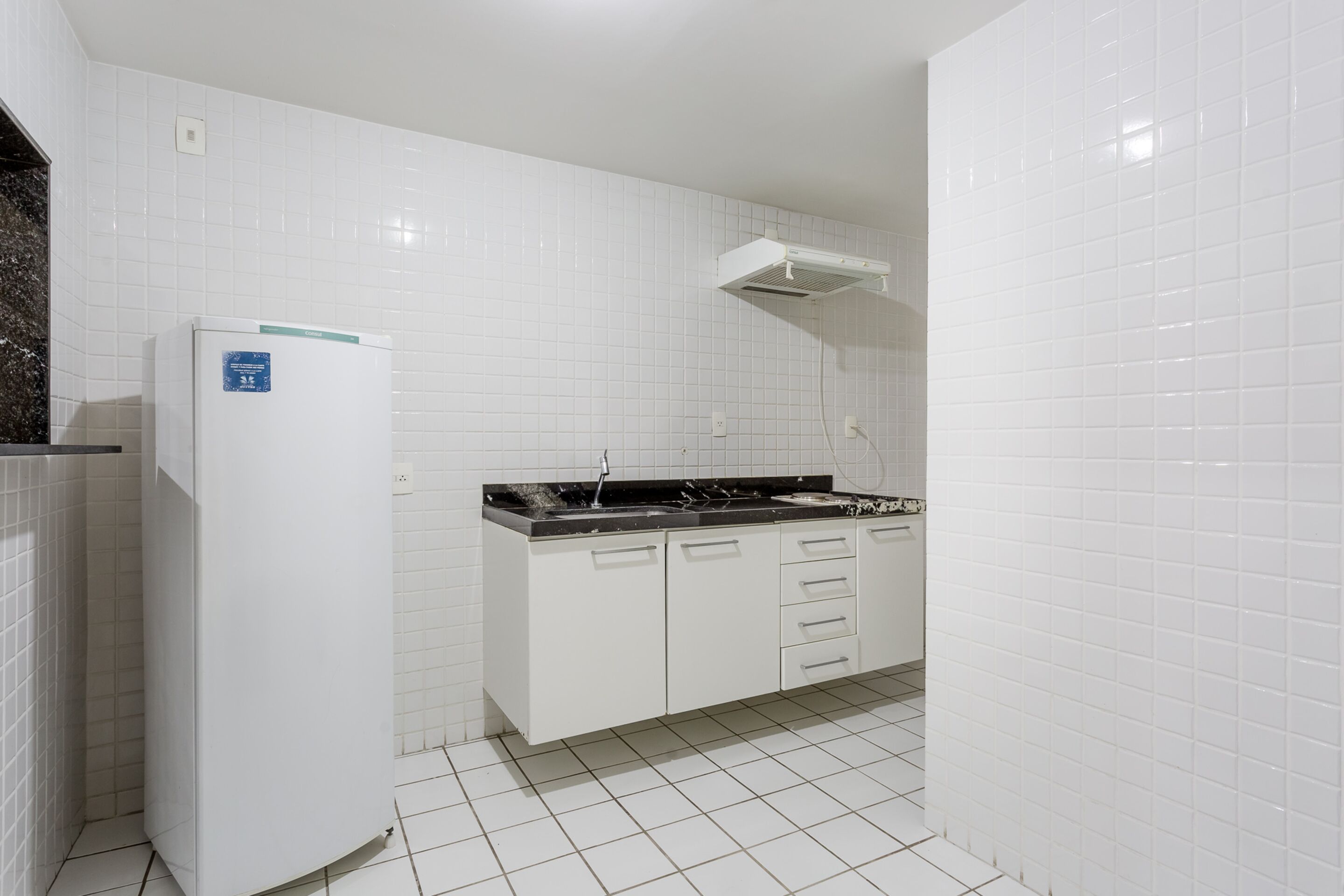 A kitchen with white cabinets, a black countertop, and a white refrigerator.