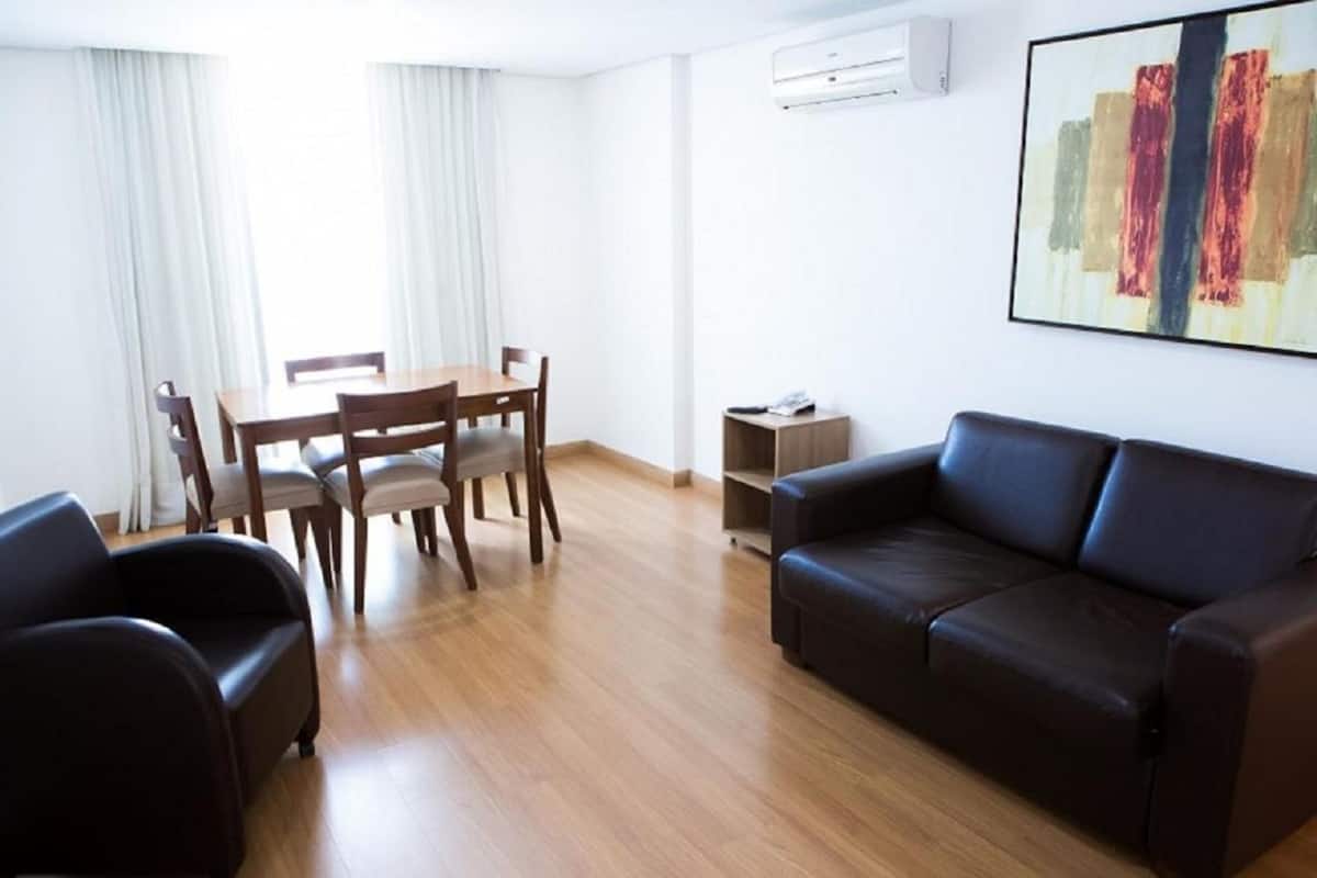 A modern living room with a wooden dining table, two chairs, a black leather sofa, and a small side table.