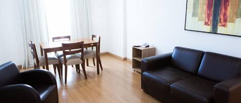 A modern living room with a wooden dining table, two chairs, a black leather sofa, and a small side table.