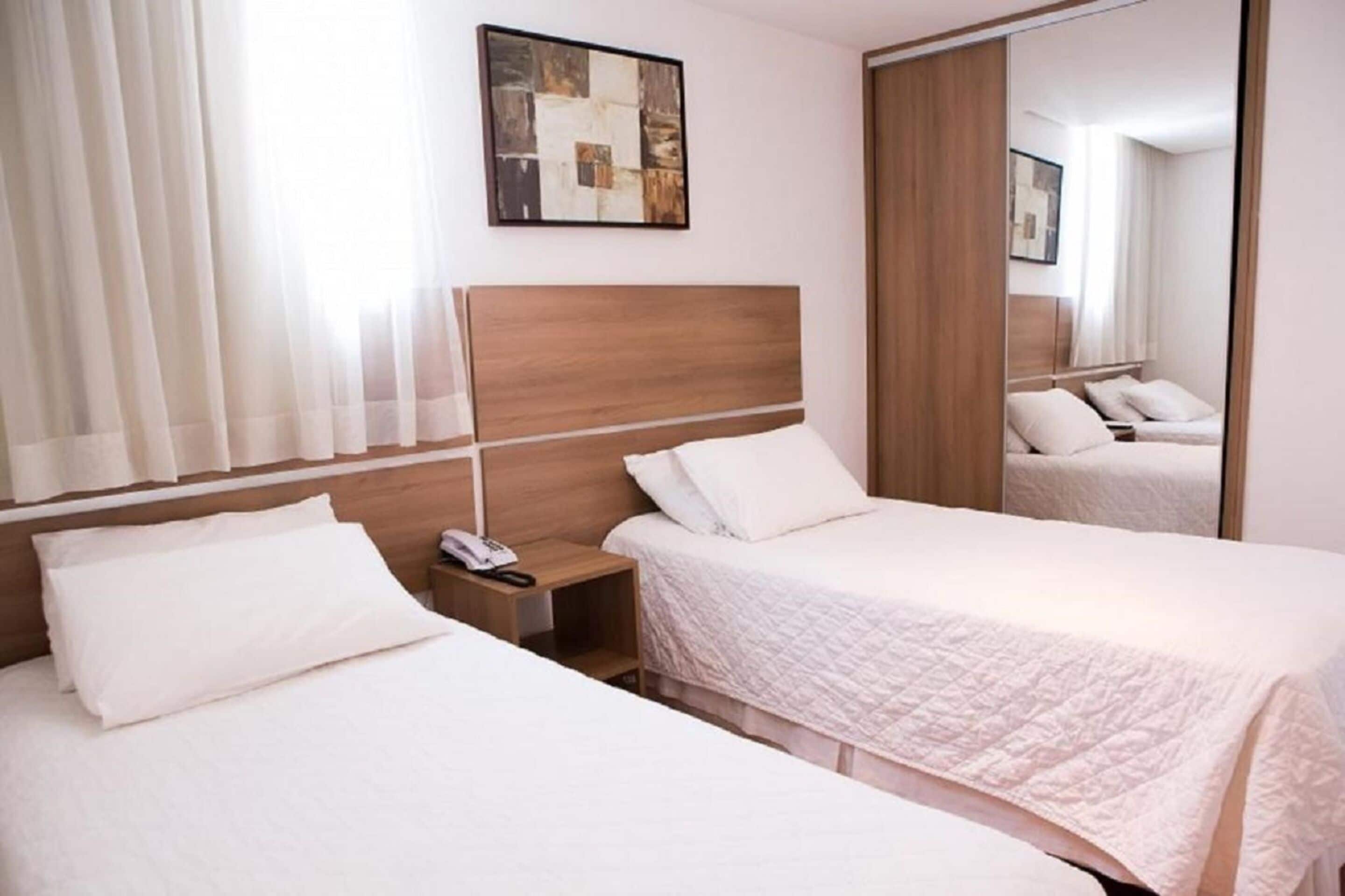 A hotel room with two beds, a nightstand with a phone, and a mirror.