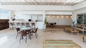 A spacious indoor area with a dining table surrounded by wicker chairs, a wooden bench, and a potted plant. - Victory Suites (Juiz de Fora)