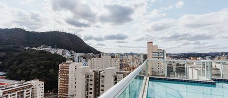 Una piscina en la azotea con vista a un paisaje urbano, rodeada de edificios altos y un fondo montañoso.